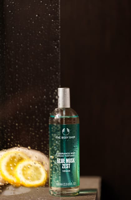 The Body Shop Blue Musk Zest bottle behind wet glass with lemon slices