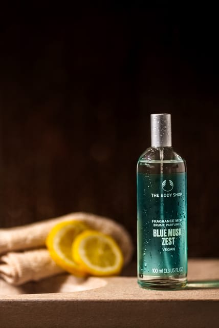 The Body Shop Blue Musk Zest fragrance mist on a stone ledge with lemon slices and a towel