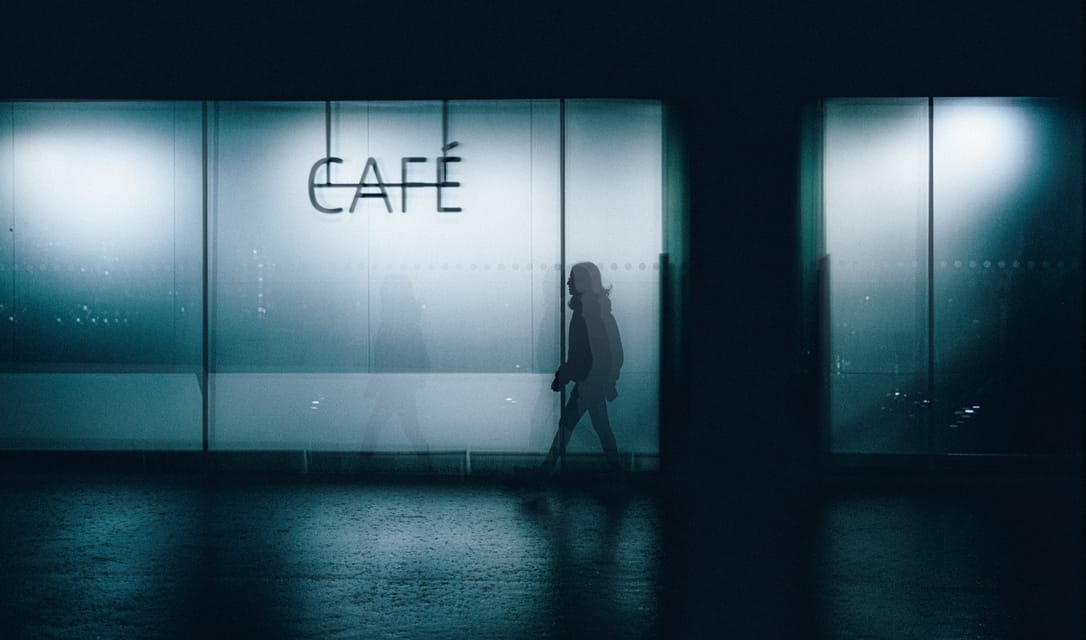 Figure passing a lit cafe facade at night