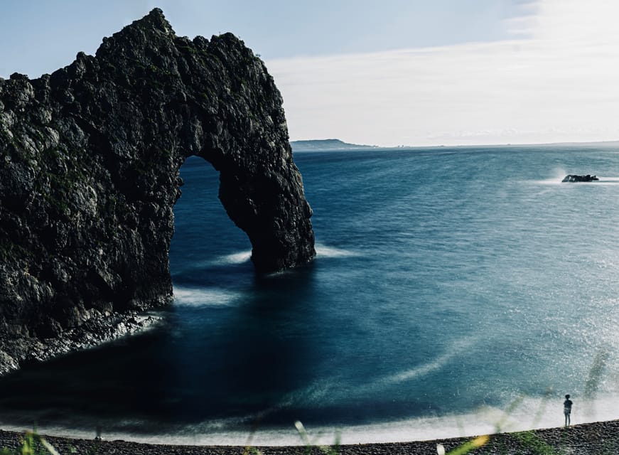 Sea arch with long-exposure water and a tiny figure on the shore
