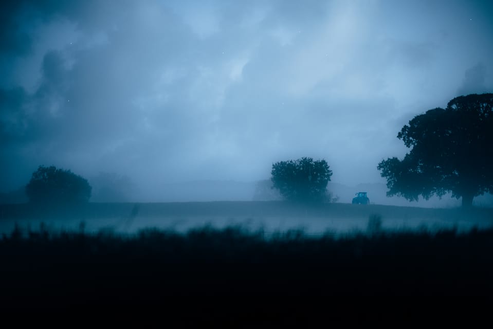 Misty field at dusk with a lone tractor