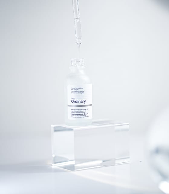 Dropper releasing serum into an open bottle of The Ordinary on an acrylic block