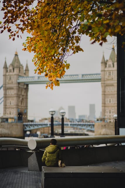 Tower Bridge framed by autumn leaves with a child on a bench